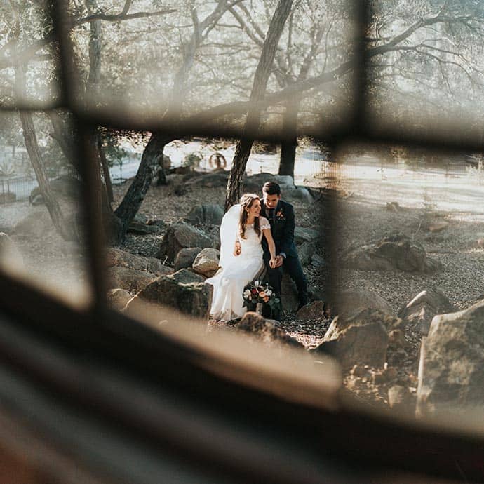 Winter Weddings Bride and Groom sitting on a rock viewed from inside a window, in a snowy wintery landscape - Camellio Wedding Planning and Events - Essex Wedding Planner